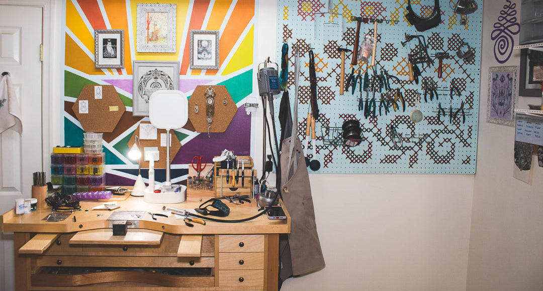 A jeweler's bench in front of a bright mural and a peg board full of hammers and various jeweler's tools.