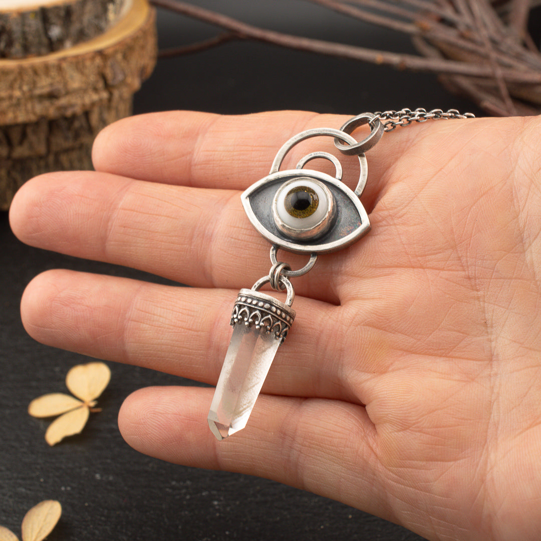 Hand holding a sterling silver glass eye pendant for protection and grounding.