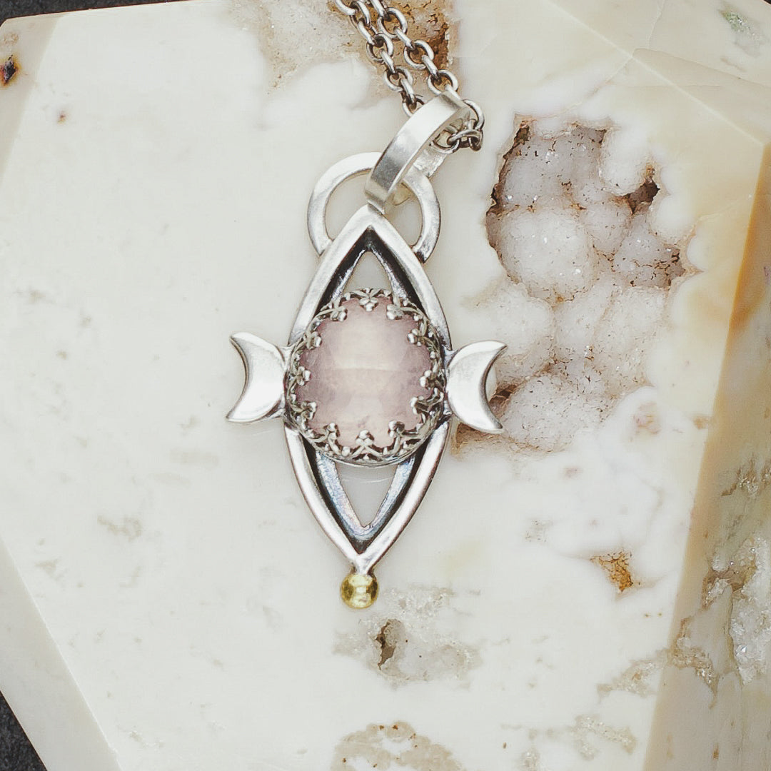 Close up detail showing gallery set rose quartz with two silver crescent moons and a gold plated detail.