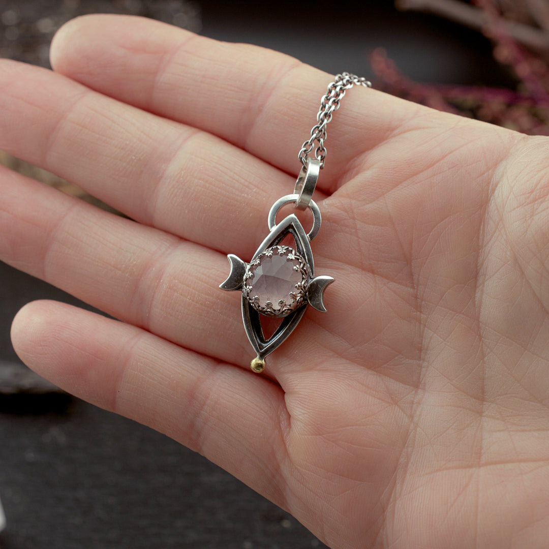 Hand holding silver and rose quartz symbolic talisman to show scale.