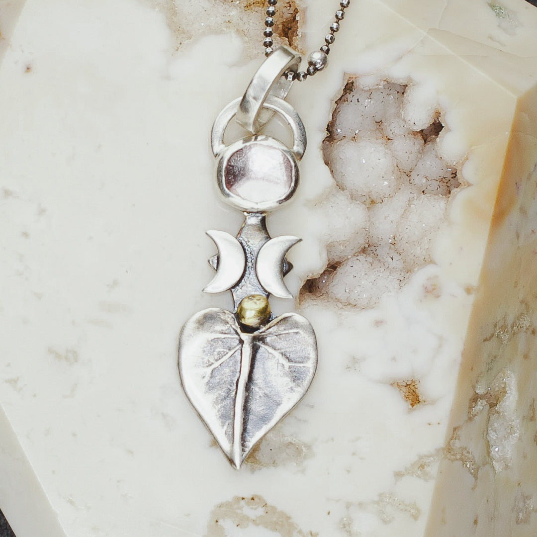 Closeup of a pink tourmaline and sterling silver talisman with gold plated detail and moons.