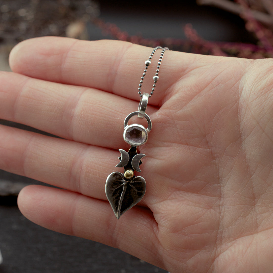 Hand holding a feminine earth witch pendant with a natural leaf and crescent moons.