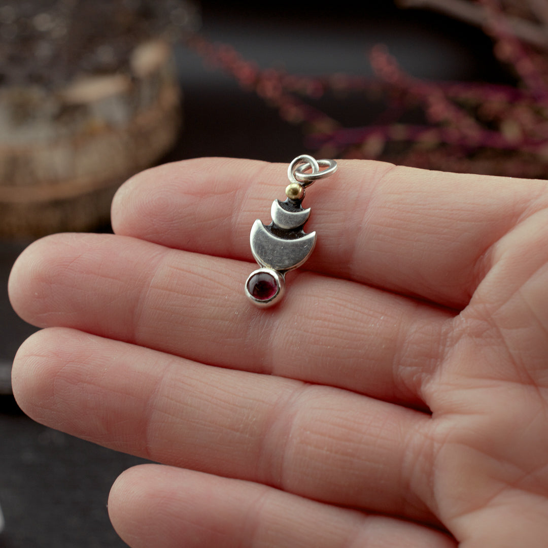 Metaphysical healing jewelry charm held in a hand to reference its tiny size.