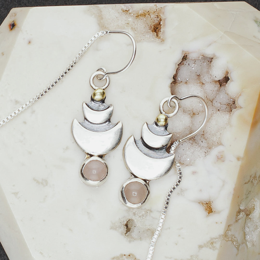 Close up of silver dangle earrings with rose quartz, moons and gold plated detail.
