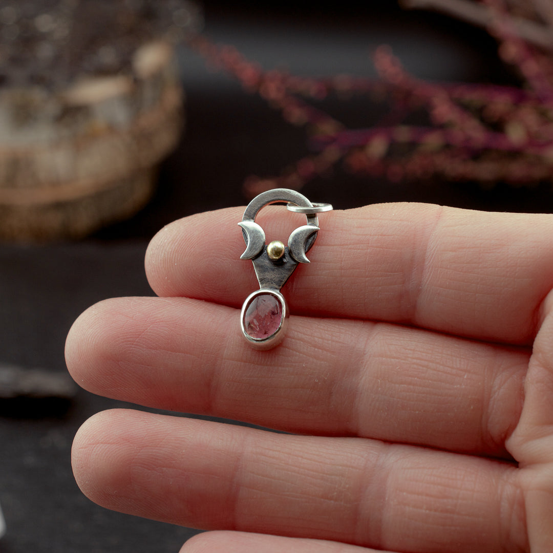 Hand holding a dainty silver charm with a natural pink tourmaline and gold plated detail