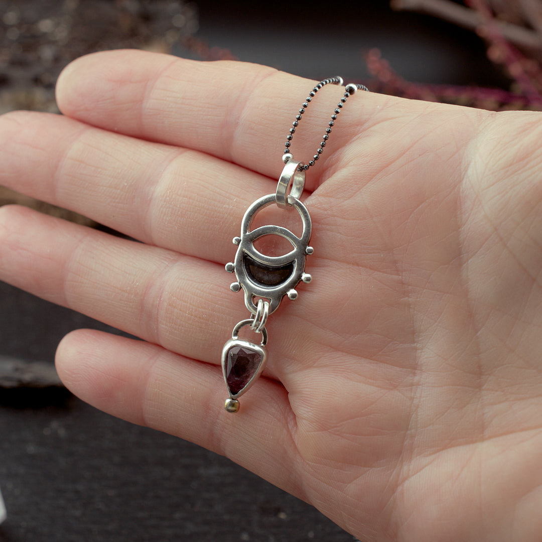 Hand holding a sacred geometry sterling silver pendant. With a pink tourmaline drop and gold plated detail.