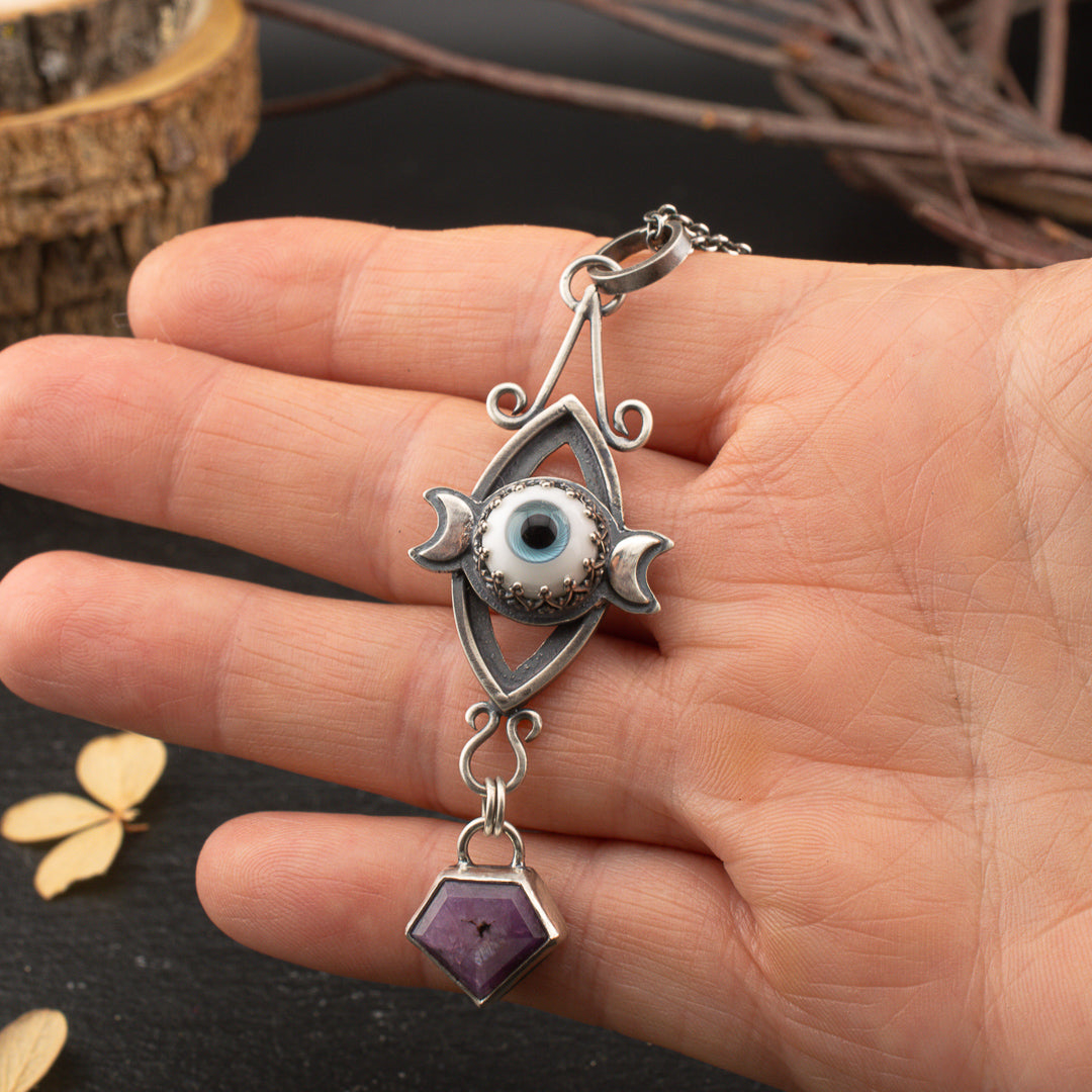 hand holding a sacred geometry pendant featuring a handmade glass eye ad a ruby.