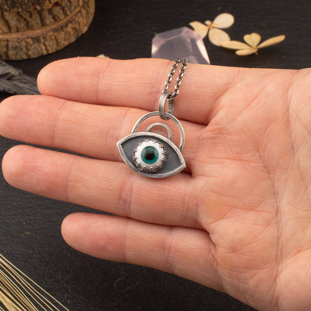 Hand holding bright teal handmade glass eye necklace in sterling silver.