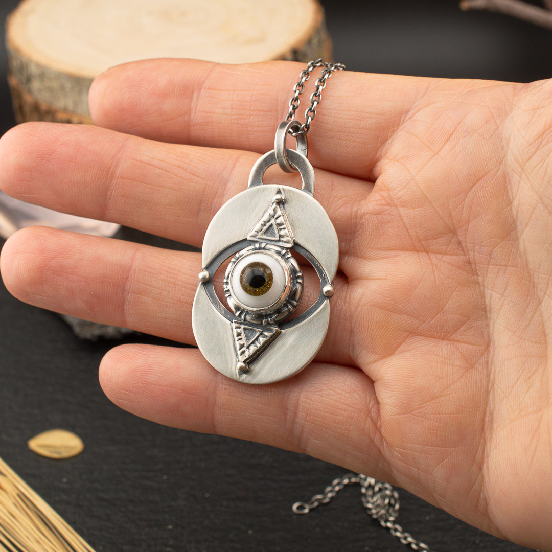 Hand holding a sterling silver stamped sigil statement necklace.