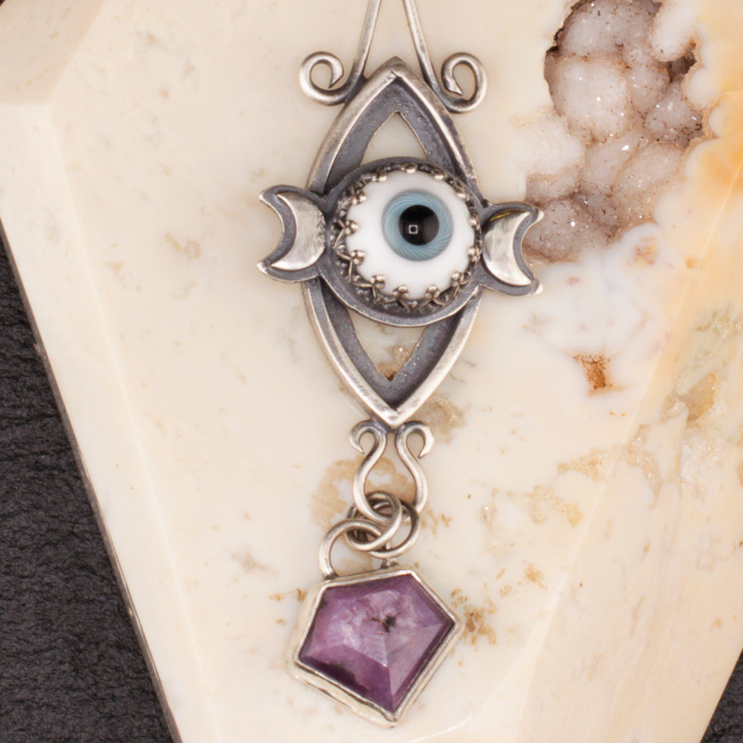 Close up of sterling silver pendant with a witch's hat and a triple goddess symbol..