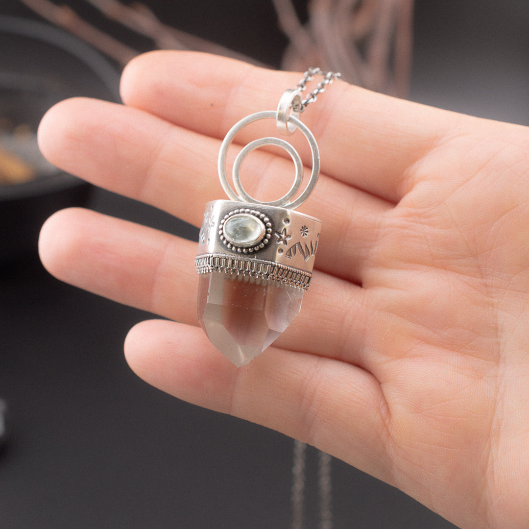 hand holding a clear quartz crystal point witha celestial stamped bezel and tourmaline.