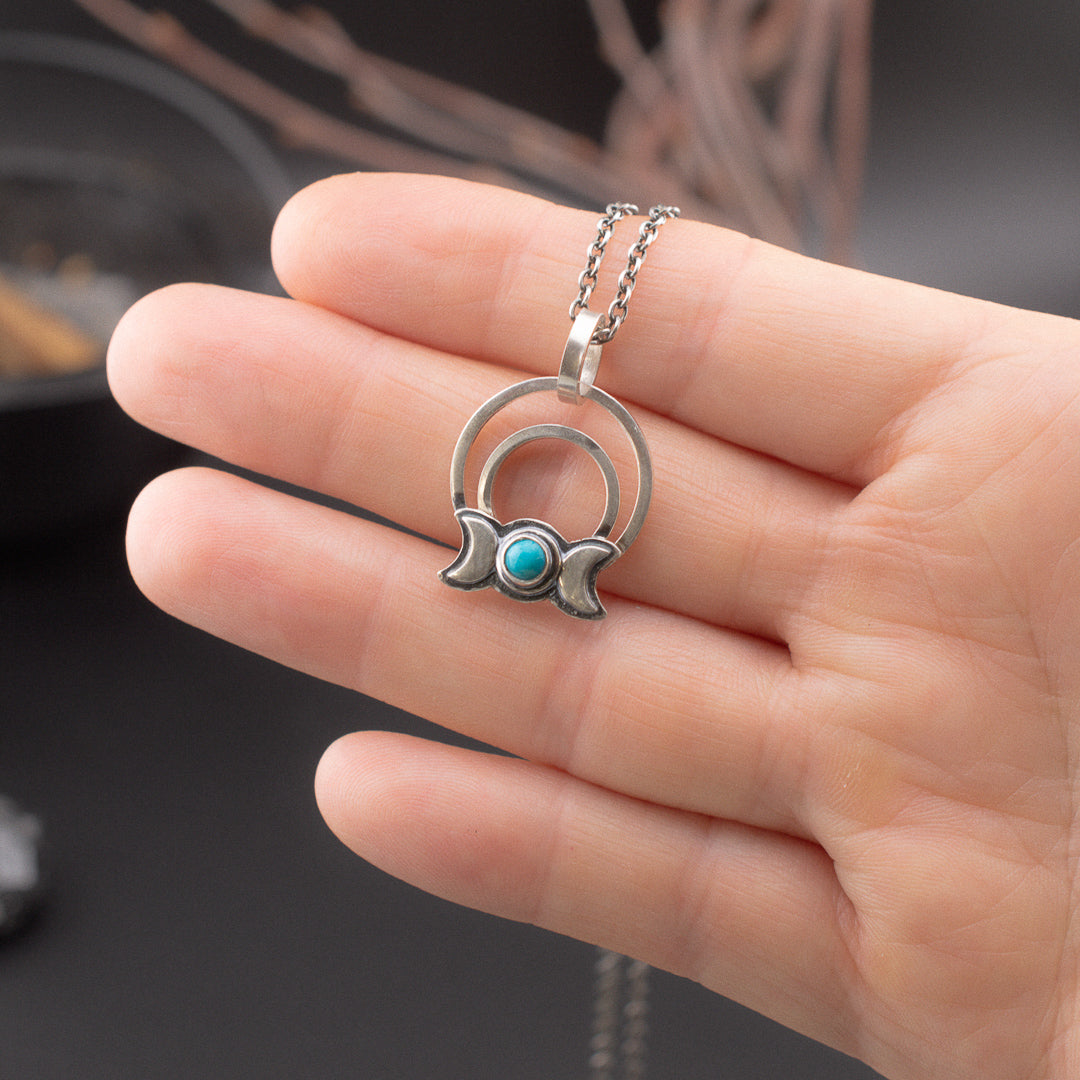 Hand holding a small triple goddess and turquoise sterling silver pendant.