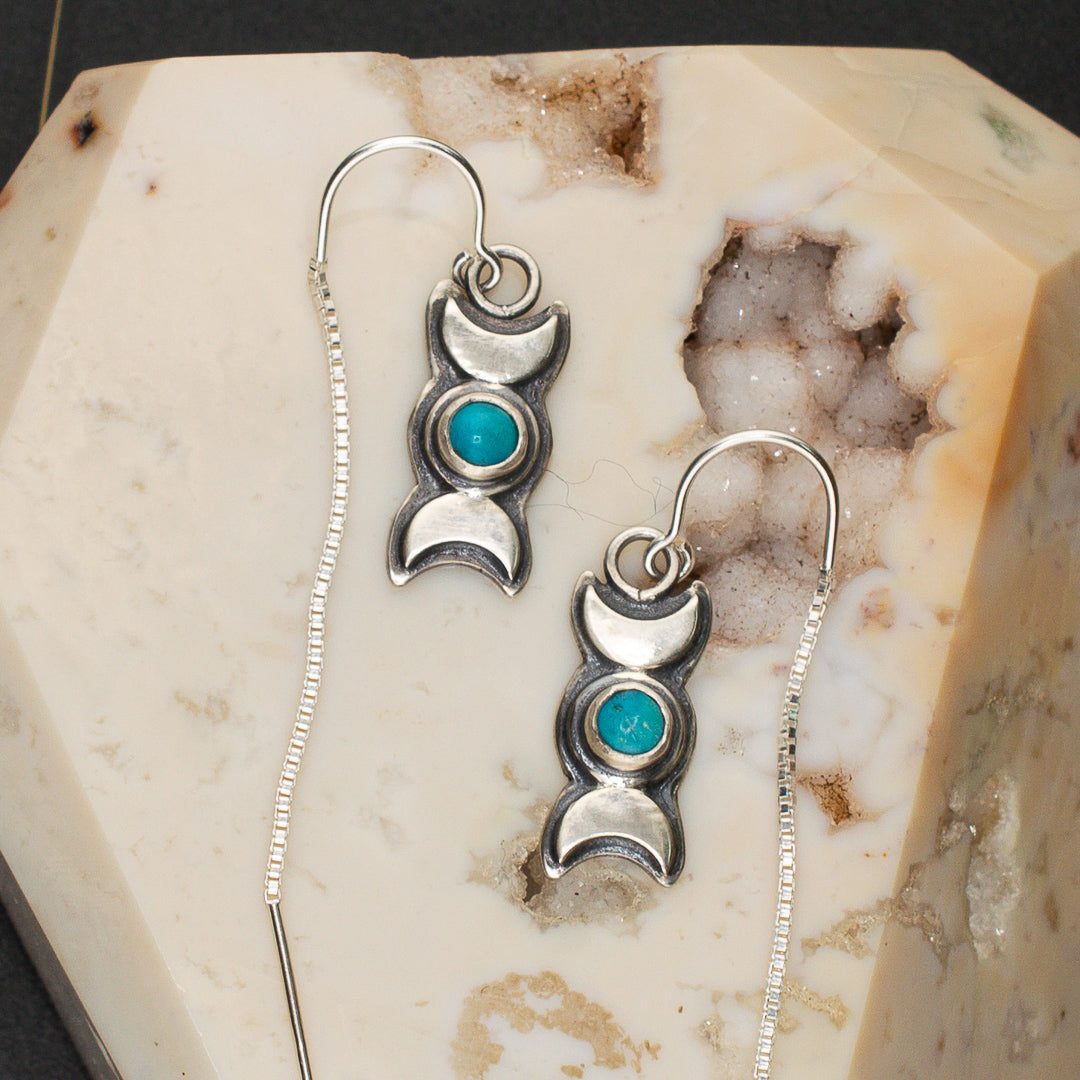 Close up of triple goddess and sturquoise sterling silver threader style earrings resting on a druzy snow agate crystal.