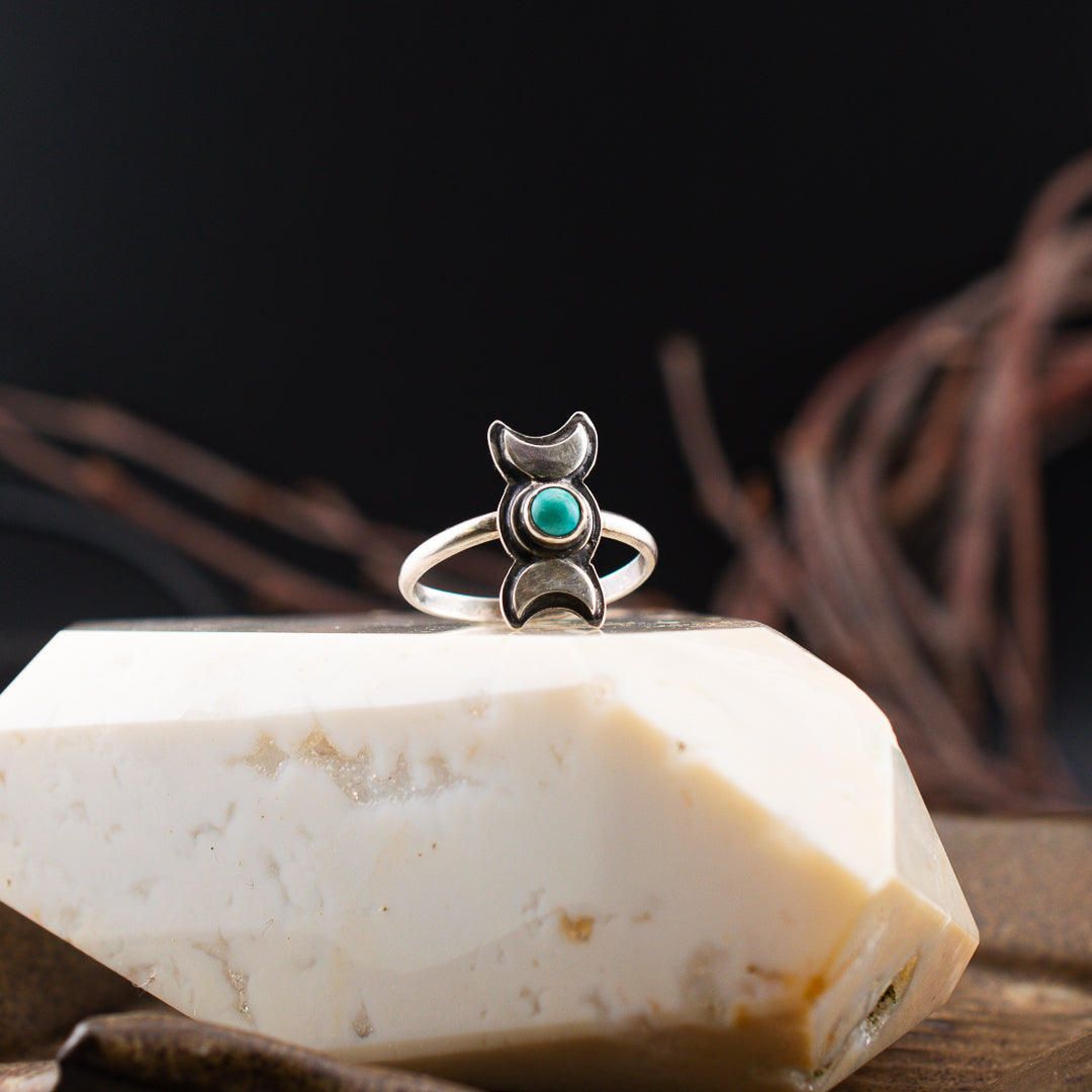 Close up shot of a delicate turquoise and moon phase ring in sterling silver sitting on a polished snow agate stone.