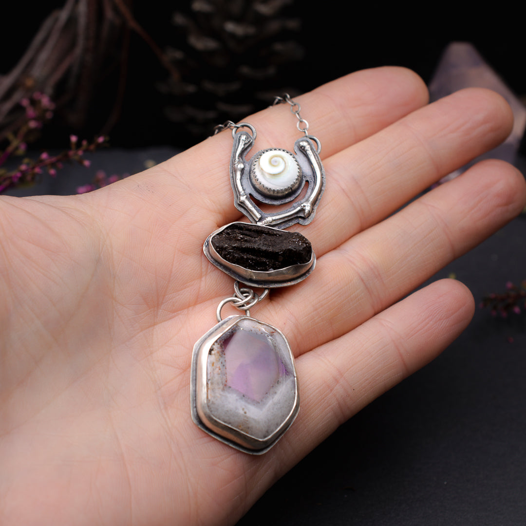 Hand holding a necklace with a shiva shell, druzy petrified wood and trapich ametyst natural gemstones set in sterling silver.