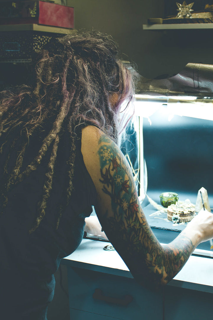 Metalsmith and artist in front of her lighbox rearranging sterling silver jewelry for a close up shot.