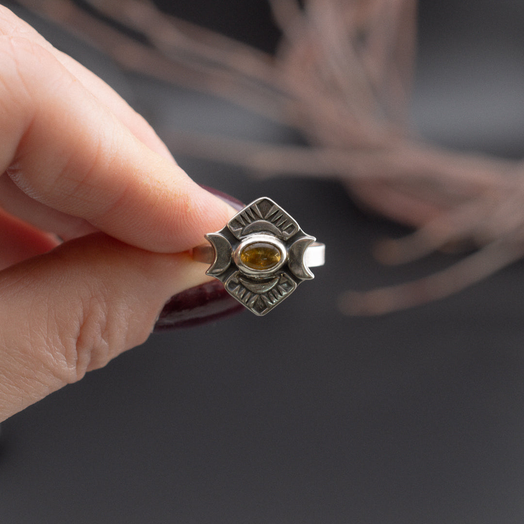 close up of a hand holding a ring with yellow tourmaline and crescent moons.