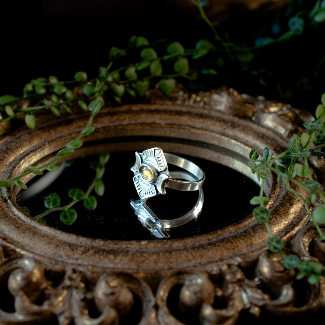 Styerling silver and yellow tourmaline ring with crescent moon details sitting on a mirror.