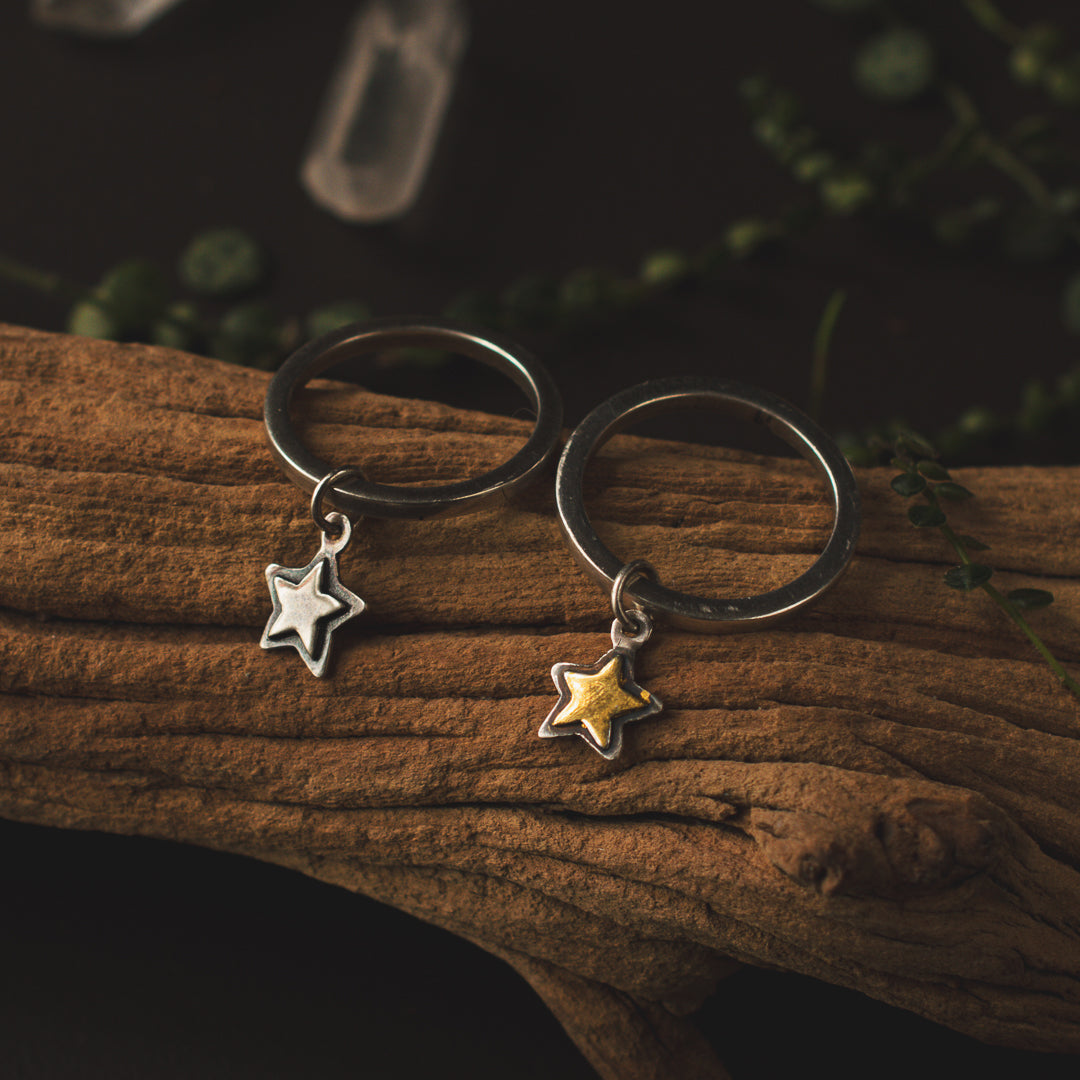 Two dainty star charm rings sitting on a piece of driftwood.