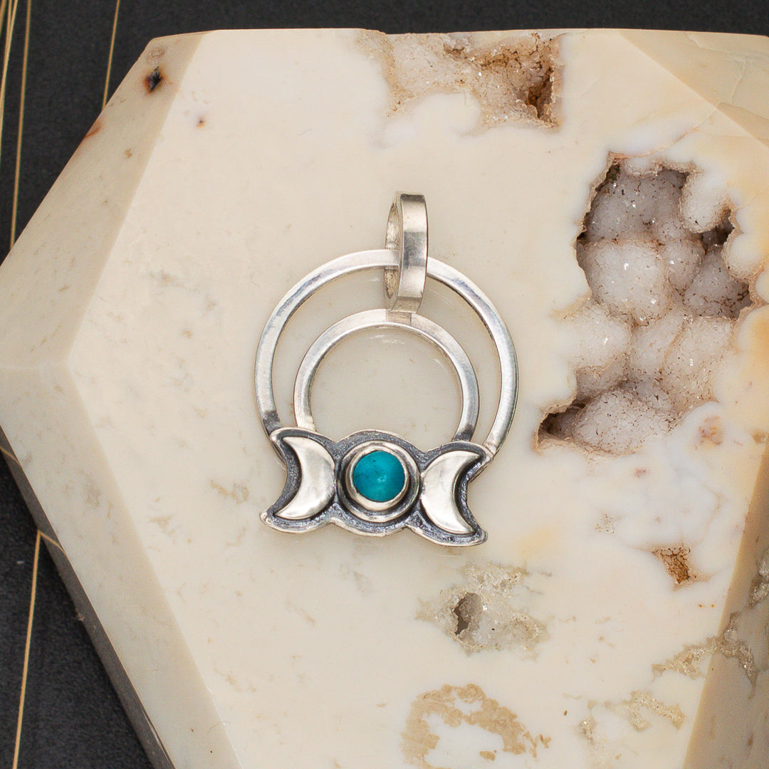 Close up  of a sterling silver and turquoise pendant featuring a triple goddess symbol.