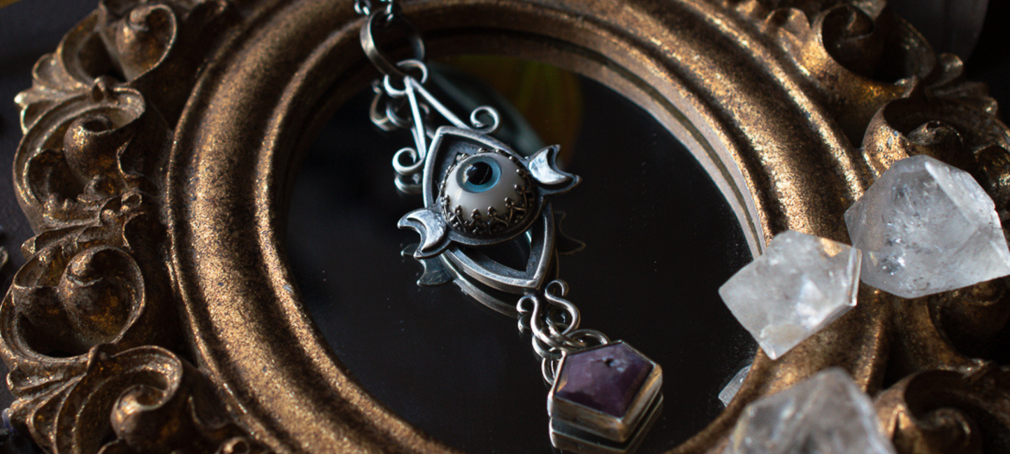 A moody closeup of an innerchild healing protective tallisman pendant laying across a gilded mirror with apophyllite crystals.