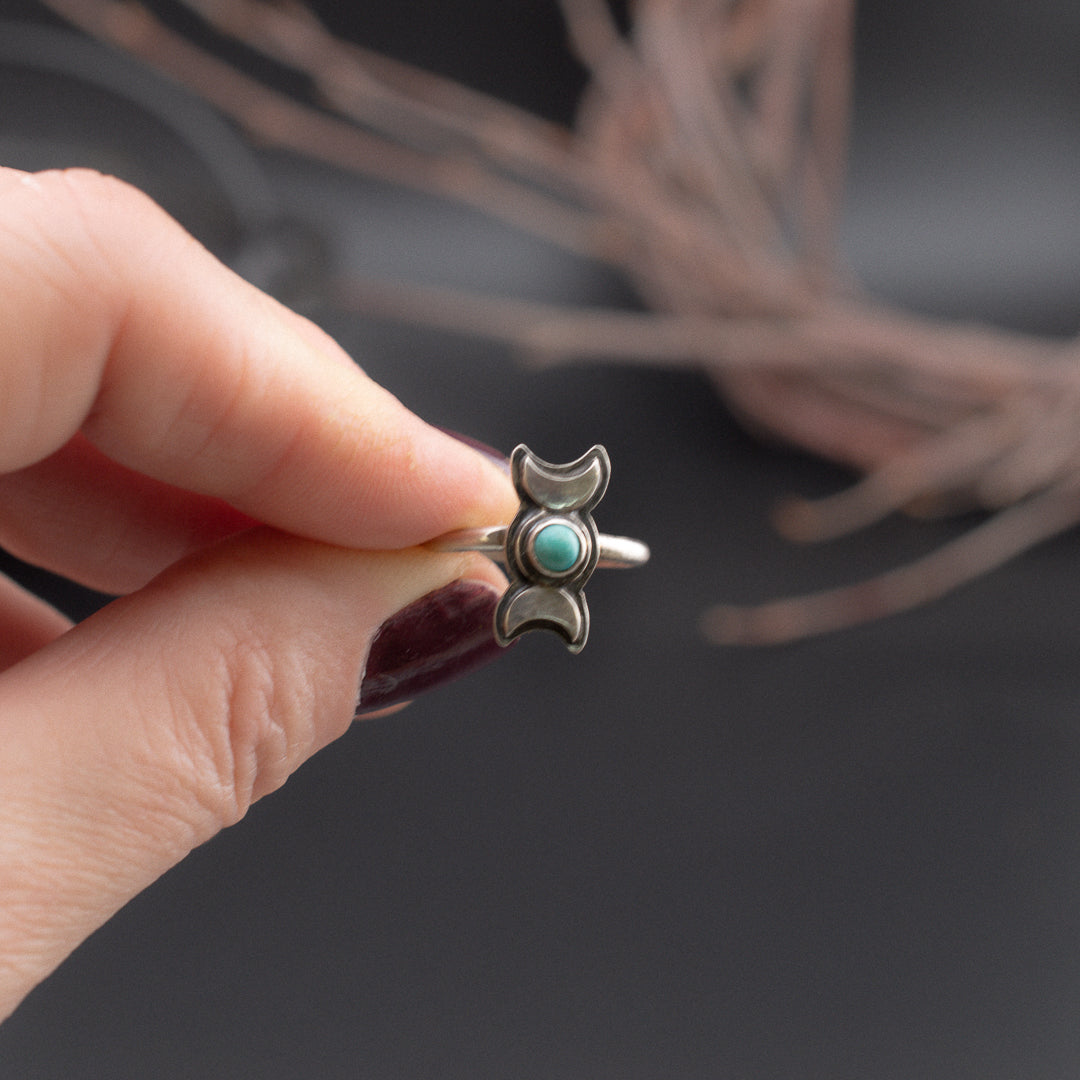 Hand holding out a sterling silver and turquoise triple goddess ring.
